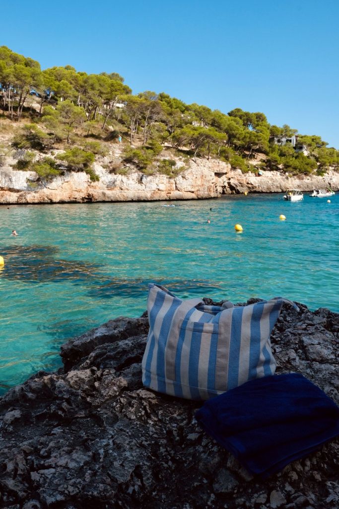 Photo by  Nik Cvetkovic - Explore Cala d'Or's stunning coastline with a blue striped bag on the rocky shore, perfect for a summer getaway.


