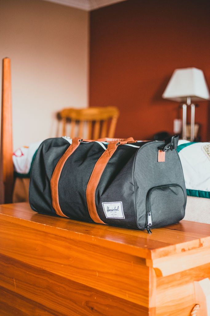 Photo by Erik Mclean -Elegant black gym bag with brown straps on a wooden table in a warm home setting. 
