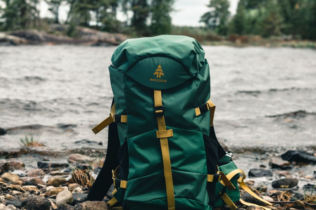 Photo by Ali Kazal- Close-up of a green hiking backpack on a rocky lakeside in Saint-Henri-de-Taillon, Quebec.

