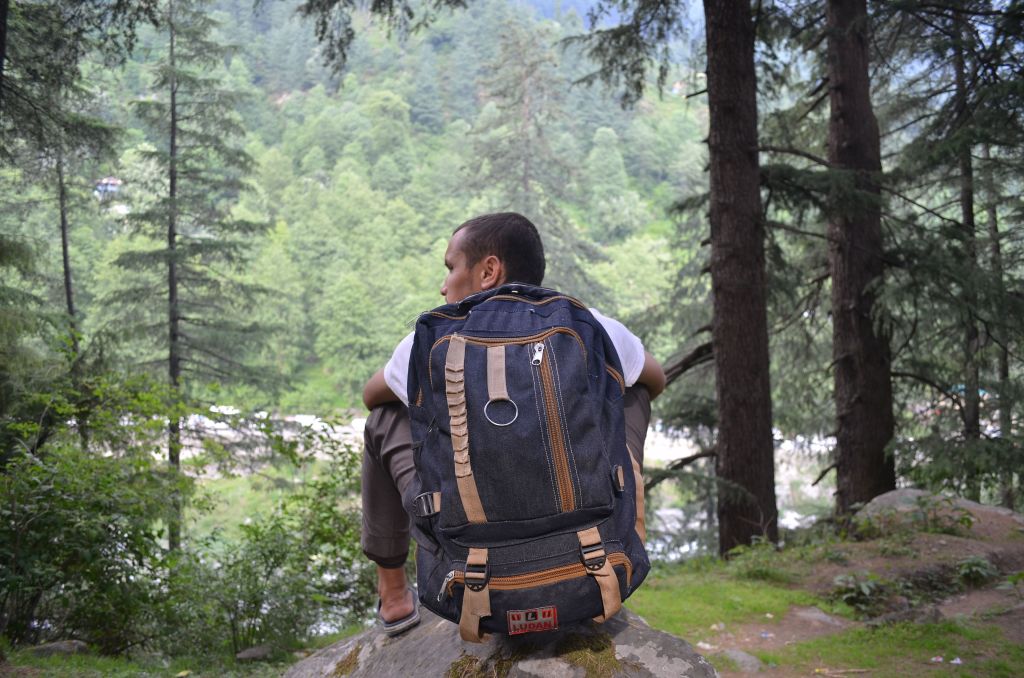 Backpacker sitting on a rock, enjoying the scenic forest and river view during a daytime hike
